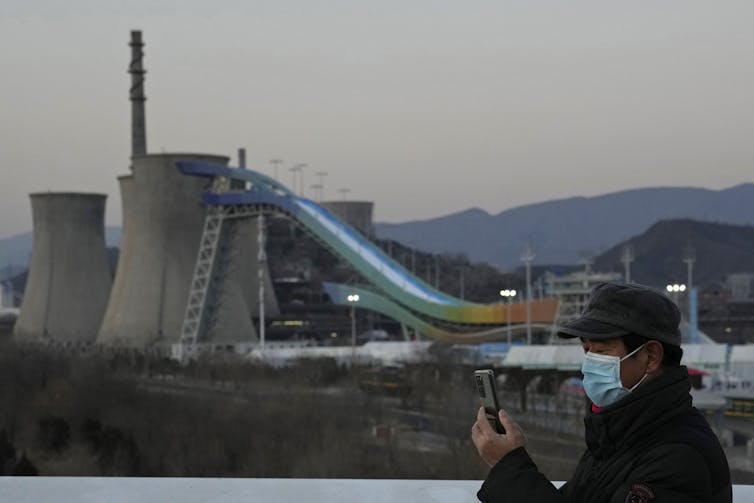 A resident wearing a mask takes photos near the Big Air Shougang, a venue for freestyle and snowboard big air events at the Beijing Winter Olympic Games.
