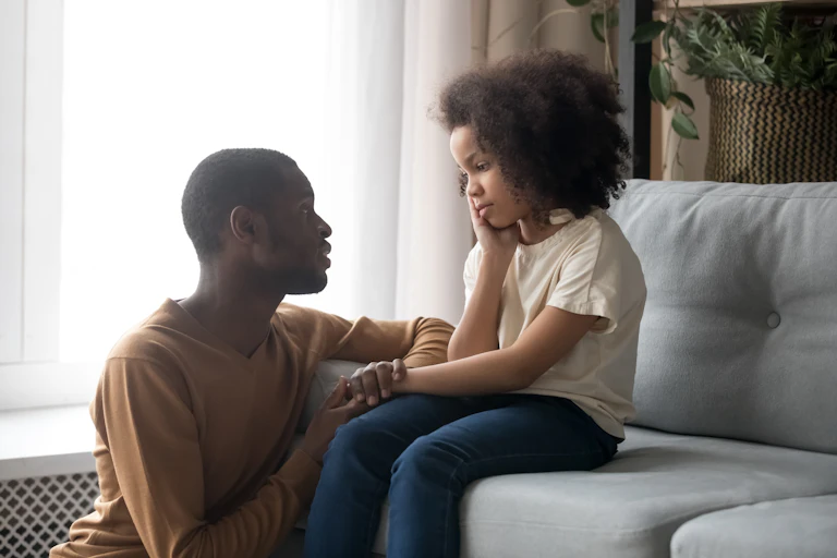 A dad and daughter sit on a couch having an intense conversation.