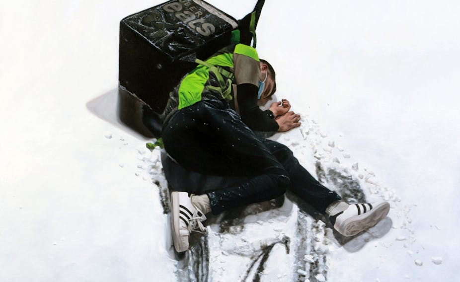 A man lies in the snow with an Ubereats backpack on his back.