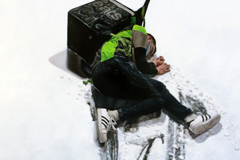 A man lies in the snow with an Ubereats backpack on his back.