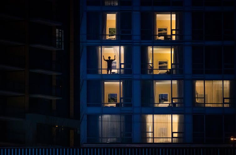 A person in silhouette is shown closing the hotel room window blinds.