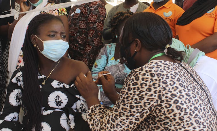 A Black woman in a mask gets a COVID-19 vaccination from a nurse.