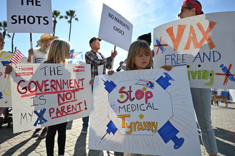 Adults and children hold protest signs while demonstrating against COVID-19 vaccine mandates.