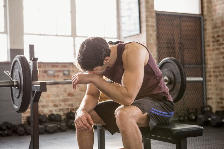 Tired man in gym clothes takes a break during his workout. Soreness after a training to failure workout may make your next workout harder.