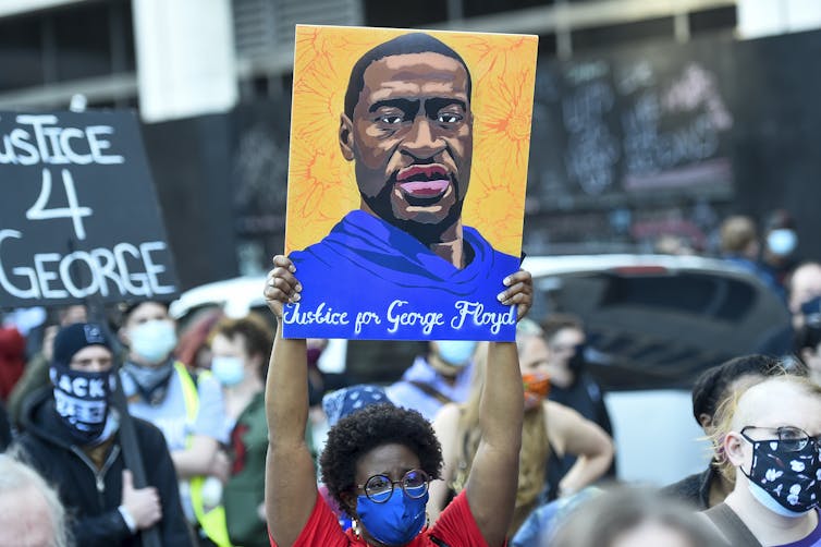 Marchers carry a poster demanding justice for George Floyd and another bearing his face.