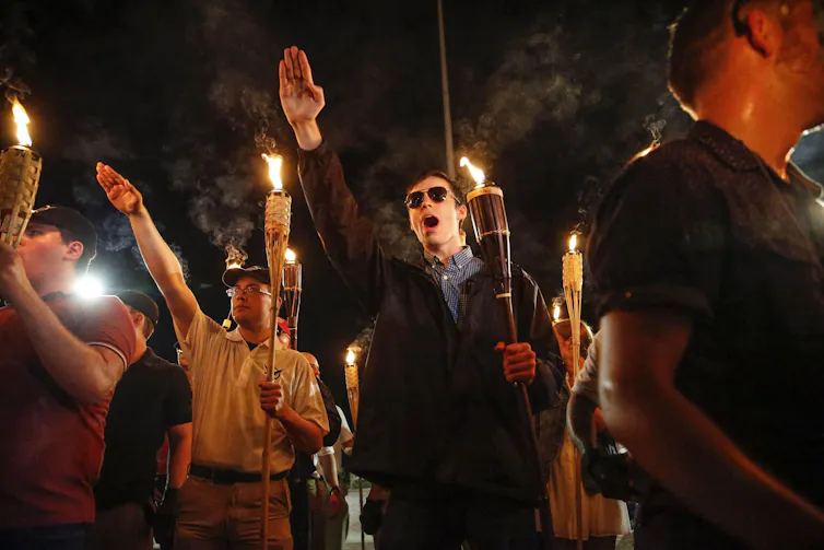 Several men carrying torches and making Nazi salutes at night.