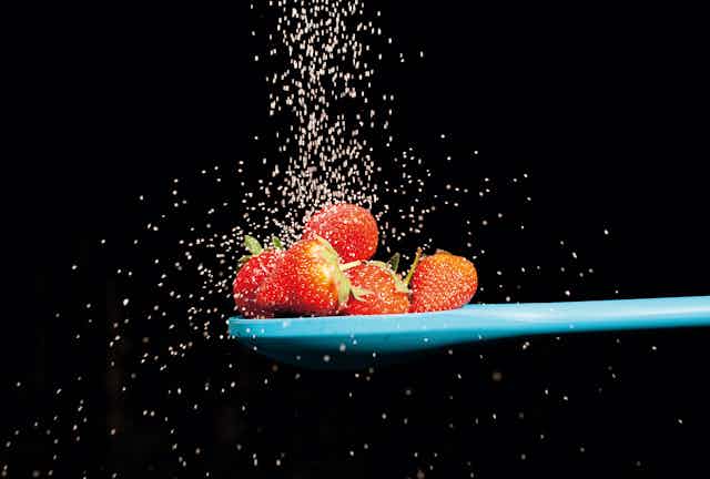 strawberries on blue spoon with sugar raining down