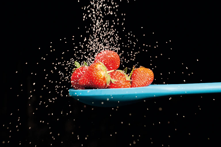 strawberries on blue spoon with sugar raining down