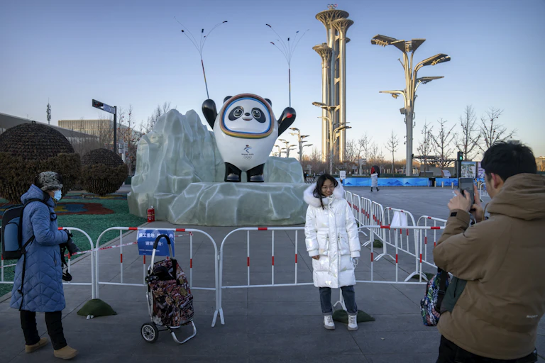 A woman poses in front of a statue of an Olympic mascott. She's wearing a big white jacket.