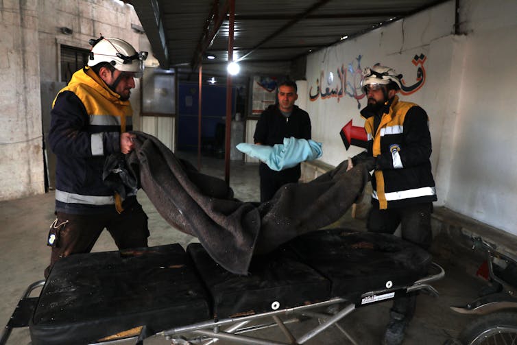 Men wearing white helmets sort bagged bodies of victims of an airstrike, including a small body of a child.