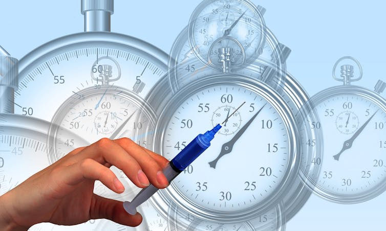 A hand with a syringe in it with stopwatches in the background