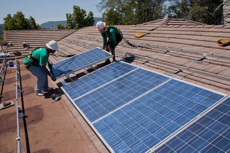 Two men installing solar panels on a rooftop
