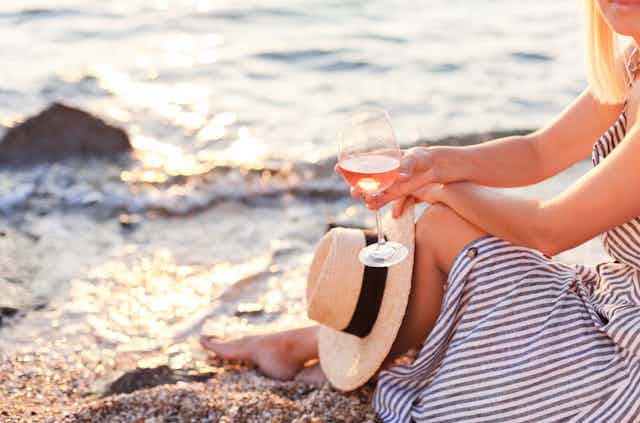 A woman drinks wine on the beach because why not