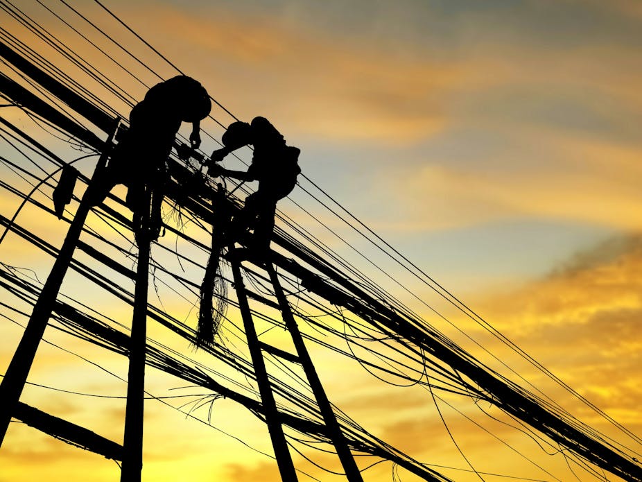 Low angle view of silhouette men working on power cables against orange sky.