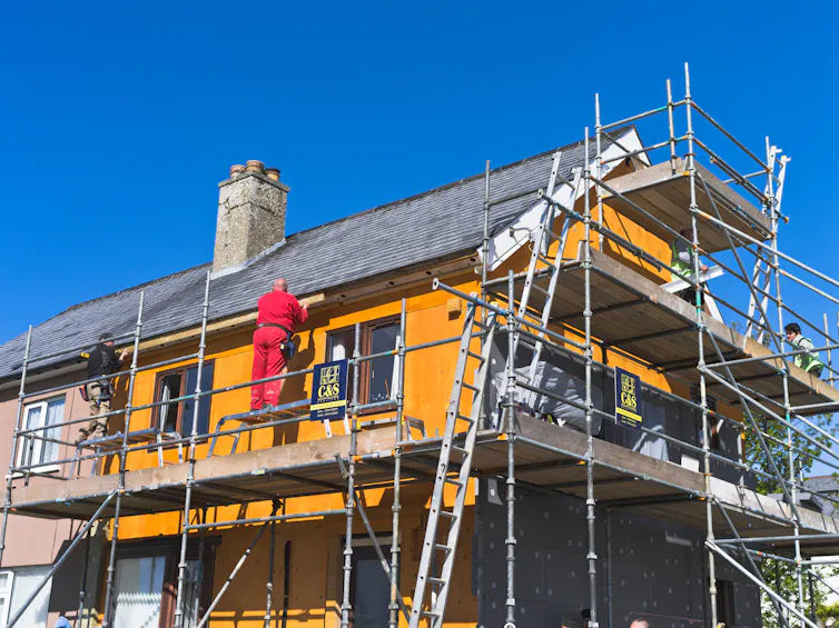 Scaffolding surrounds an orange house under blue sky.