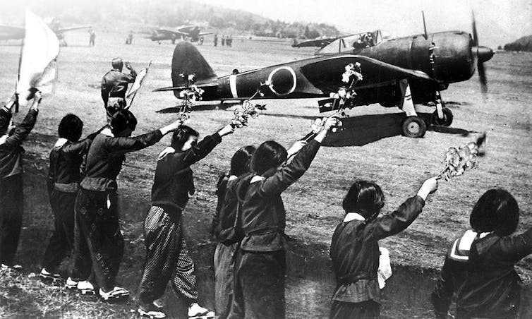School children wave as a Japanese kamikaze pilot takes off on a suicide mission in a warplane.