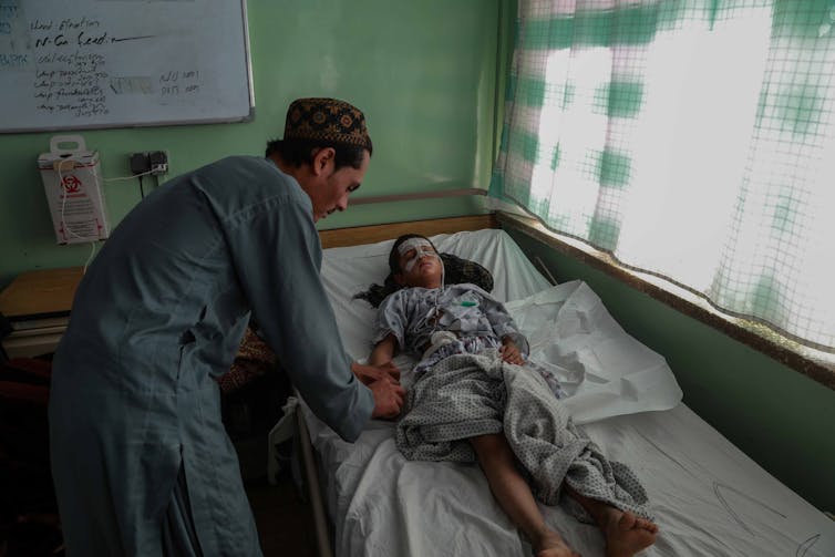A young boy lies wounded on a hospital bed with a doctor tending to his wounds.