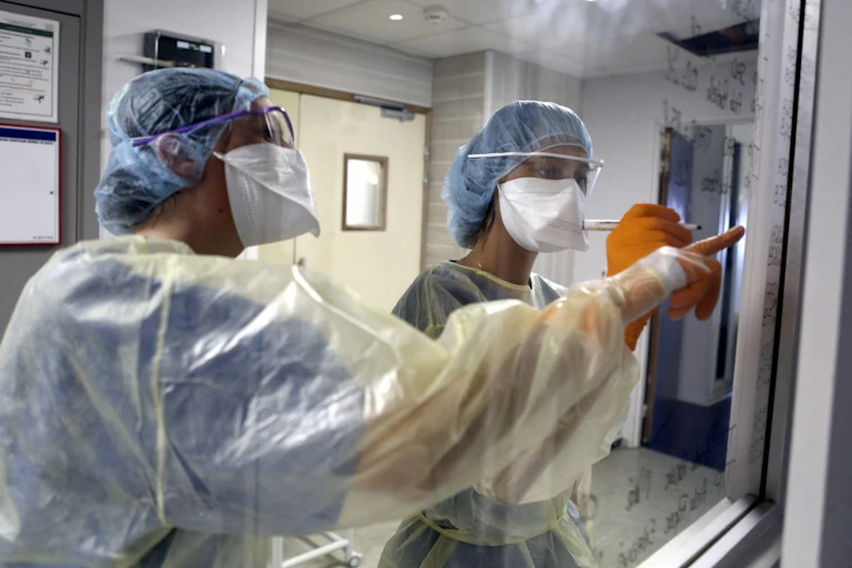 Deux soignants en tenue de protection complète sont en train de s'organiser.