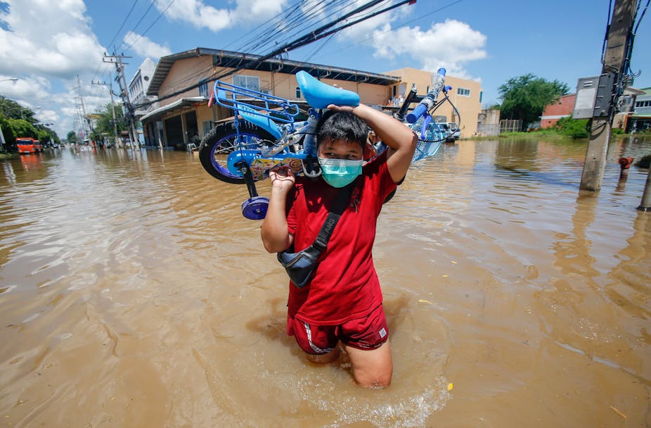 A person carries a child's bike through flood water