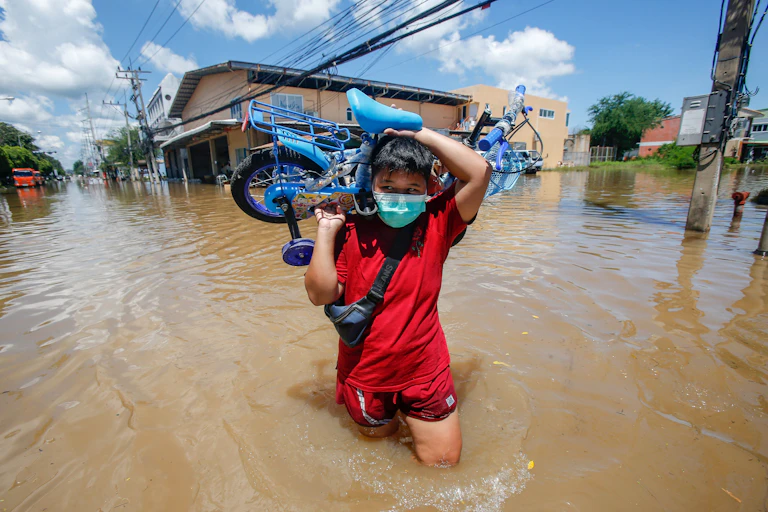 A person carries a child's bike through flood water