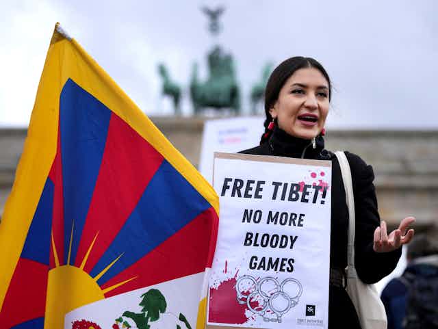 A woman stands holding a sign that reads 'Free Tibet! No more bloody games!' 