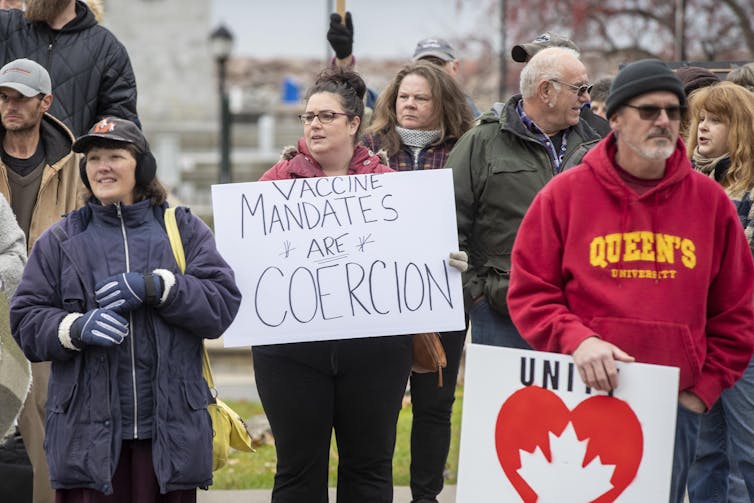 People protesting vaccine mandates. One holds a sign reading 'Vaccine mandates are coercion'