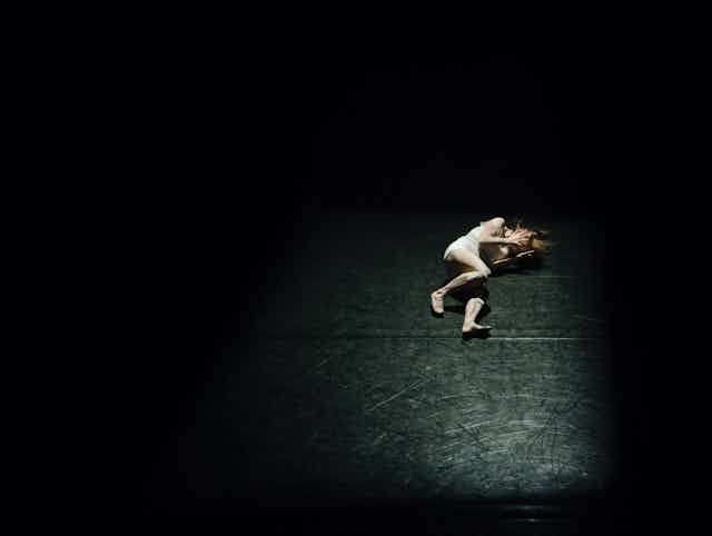 A lone dancer lies on a stage