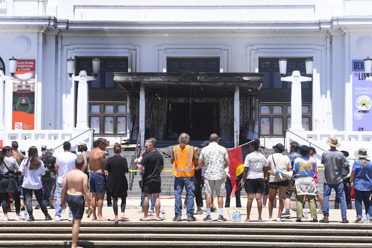 Protesters stand in front of the burned out entrance doors to Old Parliament House in Canberra