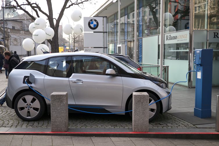 An electric car charges outside a shop