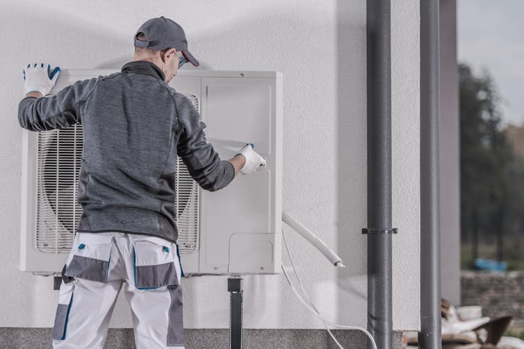 An engineer installs a large fan unit on the exterior of a house.