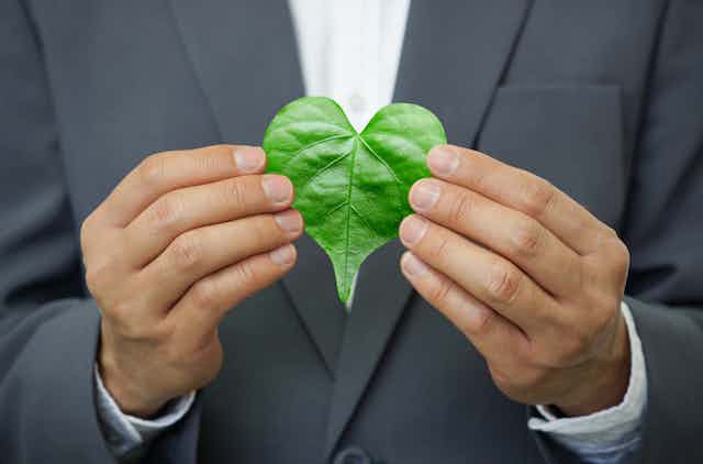 Un hombre trajeado muestra una hoja verde en forma de corazón.