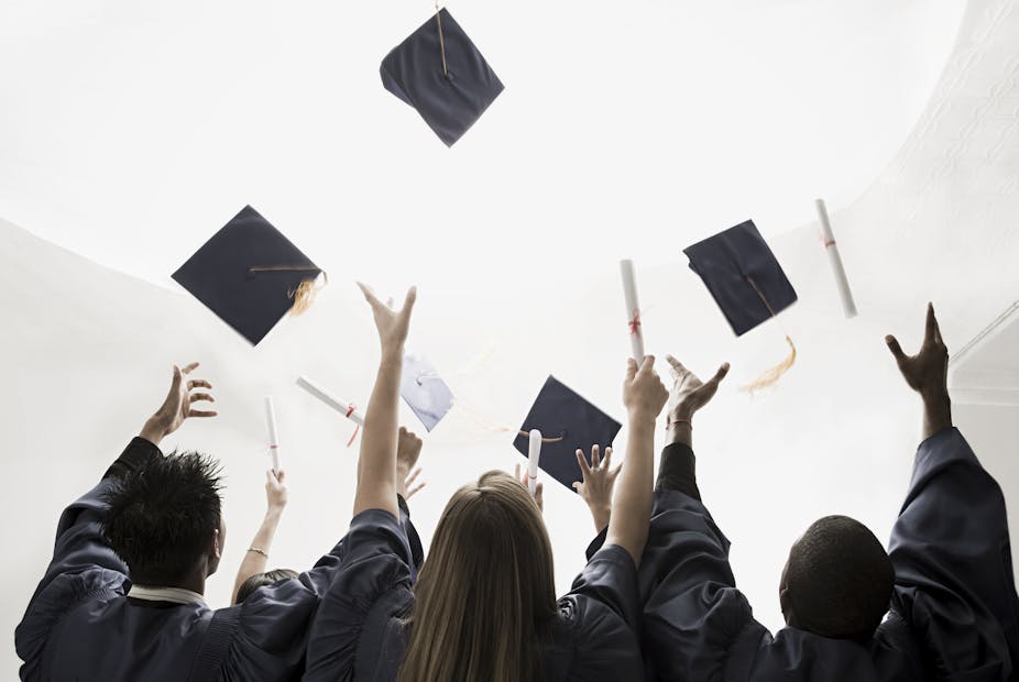 Graduating students, seen from the back, throw their mortarboards in the air.