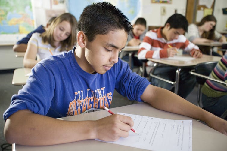 A teenage boy in a blue shirt works on an assignment in class.