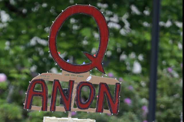 a cardboard sign displaying the letter Q above the word anon 