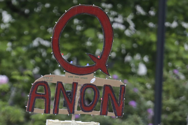 a cardboard sign displaying the letter Q above the word anon