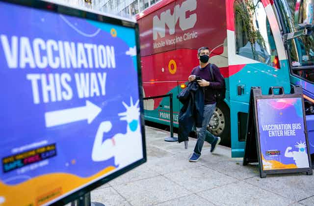 A man walks out of a vaccination bus at a mobile vaccine clinic in Midtown Manhattan with a sign that says 'vaccination this way' in foreground