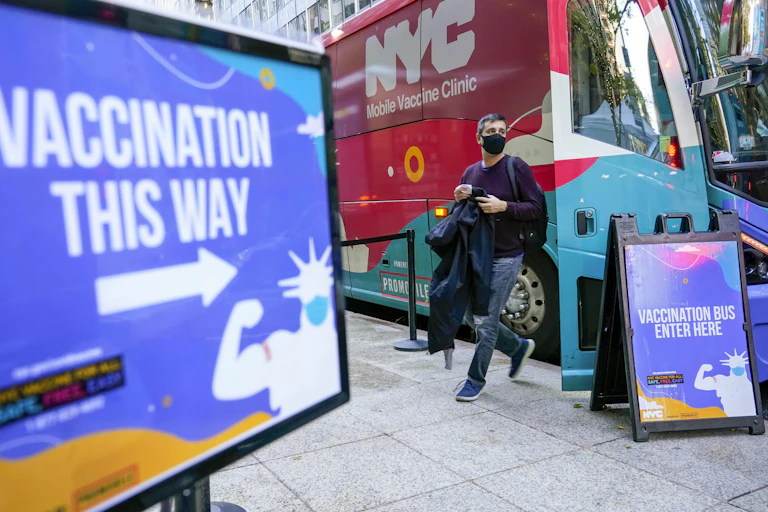 A man walks out of a vaccination bus at a mobile vaccine clinic in Midtown Manhattan with a sign that says 'vaccination this way' in foreground