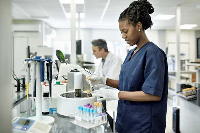 A medical lab technician in blue scrubs prepares test tubes for analysis.