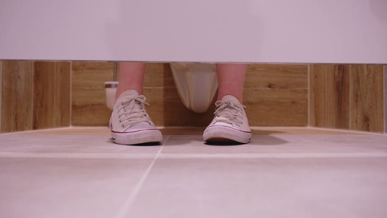 A woman's feet are seen in the stall of a bathroom.
