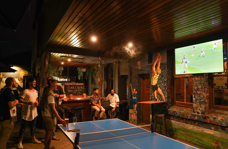 Young men watch AFL on a big screen in a pub