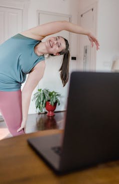 Young woman with a ponytail doing stretches while looking at a laptop screen