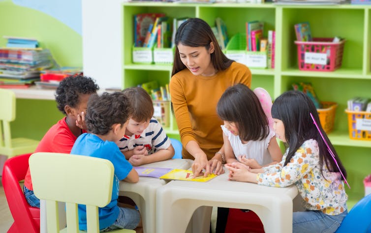 Teacher and children looking at book.