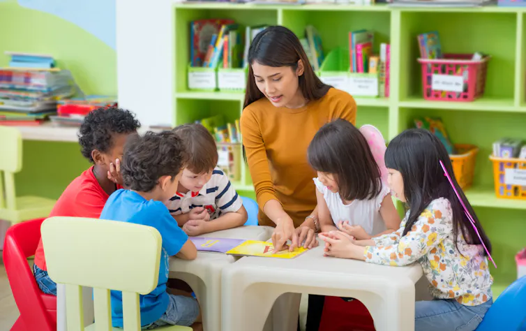 Teacher and children looking at book.