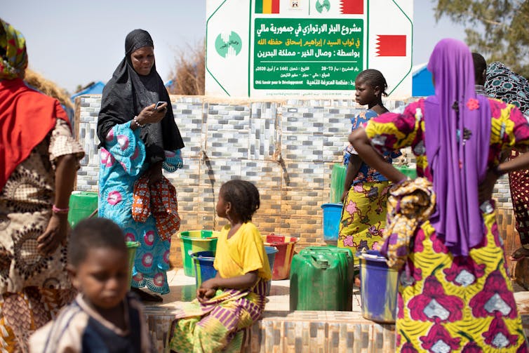Women and children collect water in buckets from taps.
