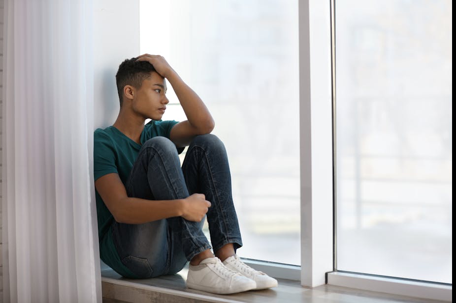 A teenage boy looking sad stares out a window.