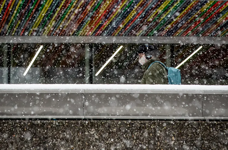 A person walks in a face mask wearing a backpack through a snowstorm.