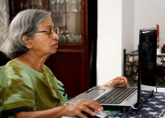 An older Asian woman works on a laptop