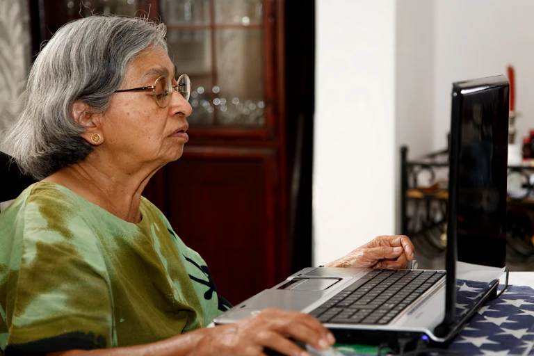 An older Asian woman works on a laptop