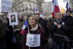 An unmasked woman carries a sign that says liberte at a protest surrounded by other protesters.