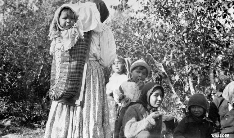 Archive photo: A woman carries her baby on her back, she's in the forest with another woman and two children.